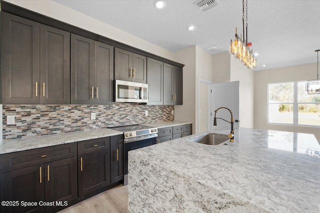 kitchen featuring appliances with stainless steel finishes, visible vents, a sink, and light stone countertops