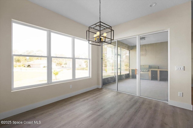 unfurnished dining area featuring an inviting chandelier, wood finished floors, and baseboards