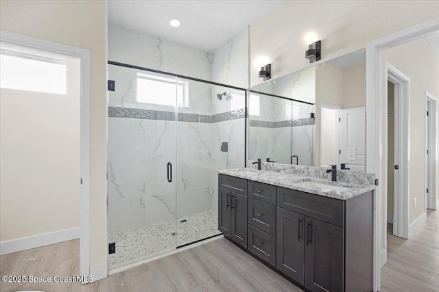 bathroom with double vanity, a marble finish shower, baseboards, wood finished floors, and a sink