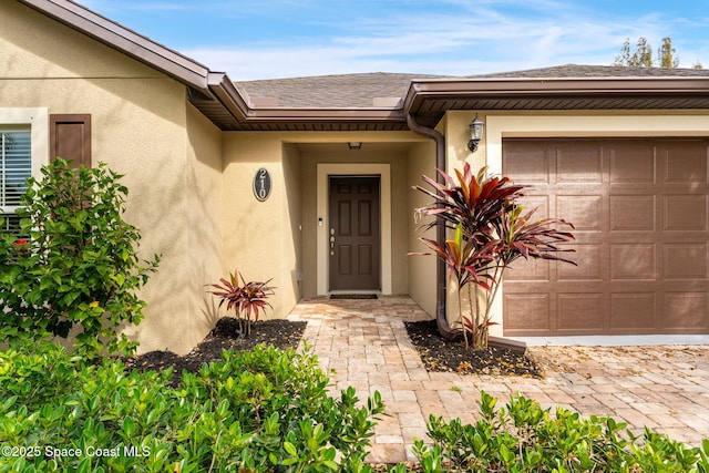 view of exterior entry featuring roof with shingles, an attached garage, and stucco siding