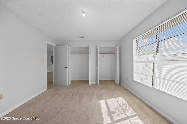 unfurnished bedroom featuring a textured ceiling, baseboards, light colored carpet, and multiple closets