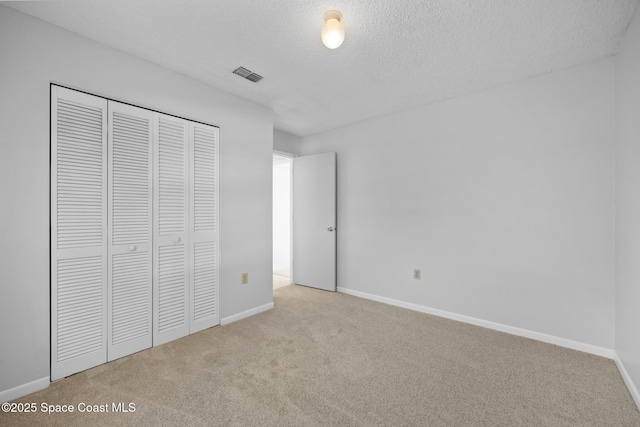 unfurnished bedroom featuring a textured ceiling, light carpet, visible vents, baseboards, and a closet