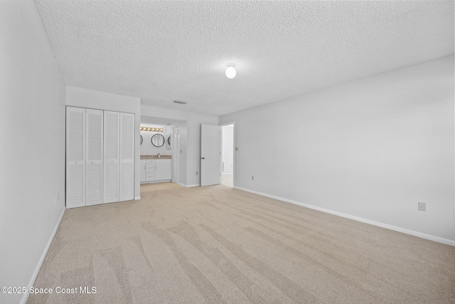 unfurnished bedroom with ensuite bath, baseboards, a textured ceiling, and light colored carpet