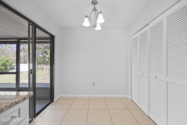 unfurnished dining area with light tile patterned flooring, an inviting chandelier, and baseboards