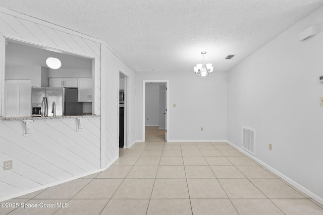 interior space featuring light tile patterned floors, a textured ceiling, visible vents, and an inviting chandelier