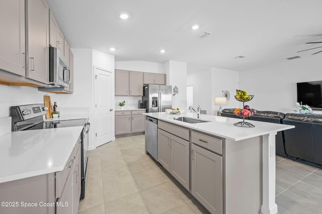 kitchen with a kitchen island with sink, stainless steel appliances, a sink, open floor plan, and light countertops