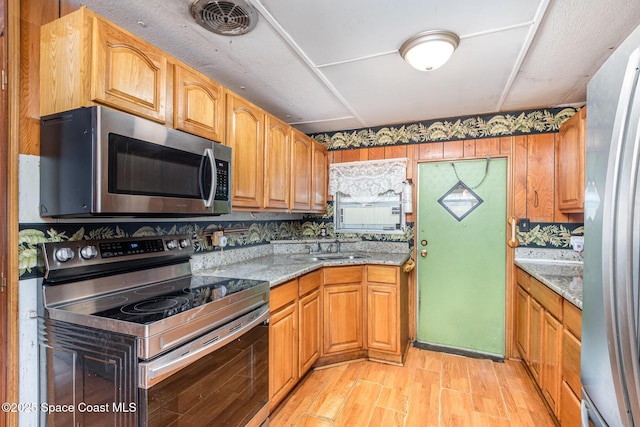 kitchen with visible vents, appliances with stainless steel finishes, a sink, light stone countertops, and light wood-type flooring