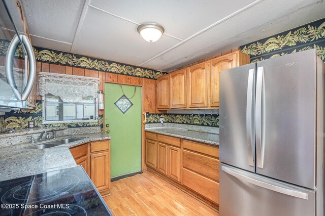 kitchen with cooktop, light wood finished floors, light stone counters, freestanding refrigerator, and a sink