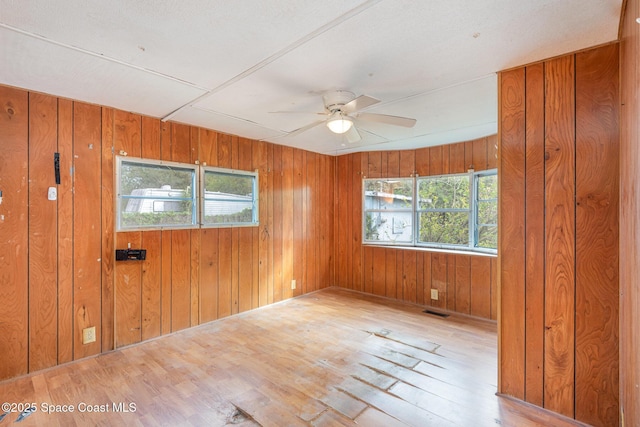 spare room featuring ceiling fan, wood walls, wood finished floors, and visible vents