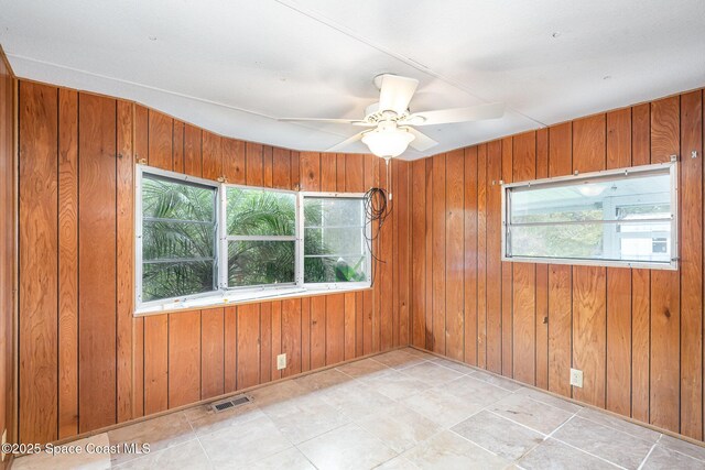 empty room with a ceiling fan, visible vents, and wooden walls