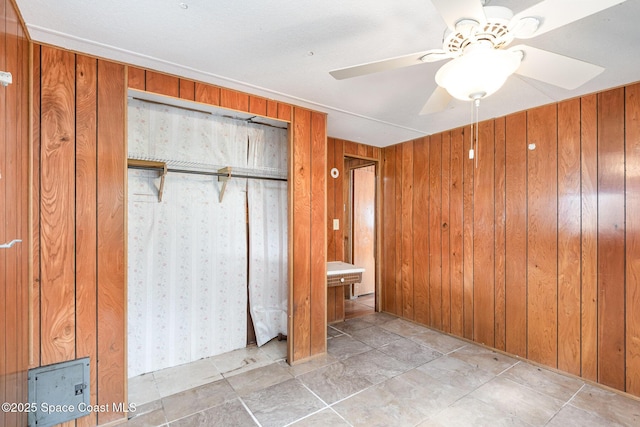 unfurnished bedroom with wood walls, ceiling fan, and a closet