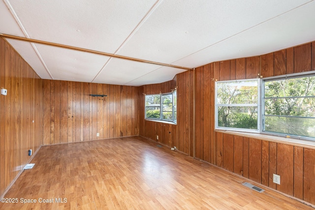 empty room with wood finished floors, visible vents, and wooden walls