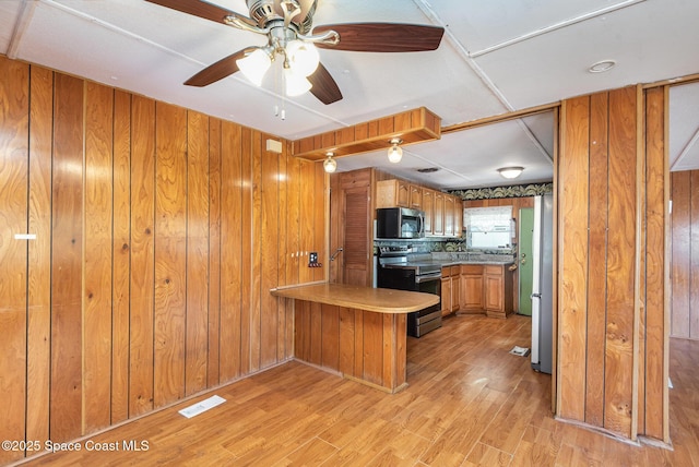 kitchen featuring a peninsula, brown cabinetry, wooden walls, and stainless steel appliances