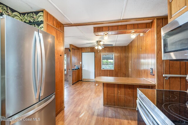 kitchen featuring wooden walls, brown cabinetry, ceiling fan, appliances with stainless steel finishes, and light wood-style floors