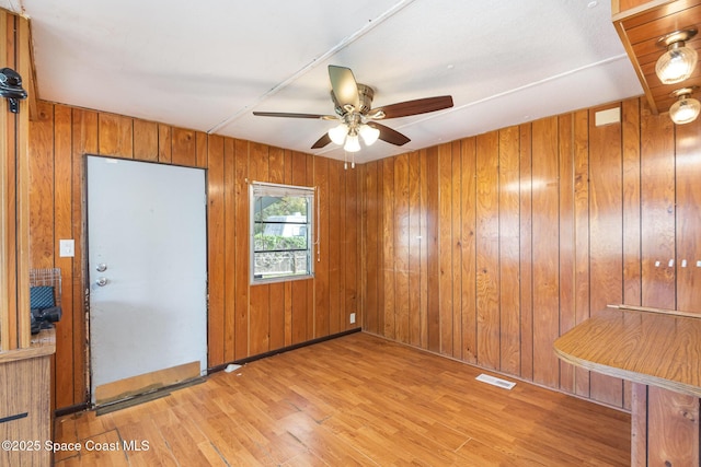 unfurnished room with a ceiling fan, wooden walls, visible vents, and wood finished floors