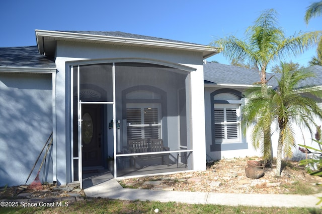 doorway to property featuring stucco siding and roof with shingles