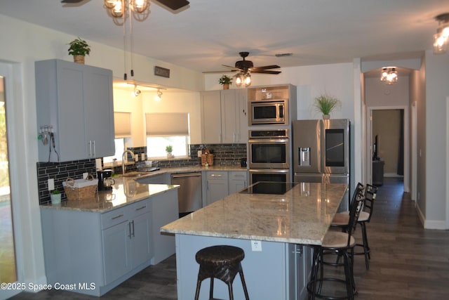 kitchen with backsplash, a breakfast bar, light stone counters, stainless steel appliances, and a sink