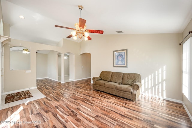 living room with arched walkways, visible vents, vaulted ceiling, and wood finished floors