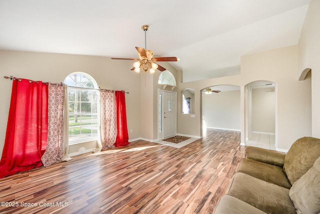 unfurnished living room featuring baseboards, arched walkways, ceiling fan, wood finished floors, and vaulted ceiling