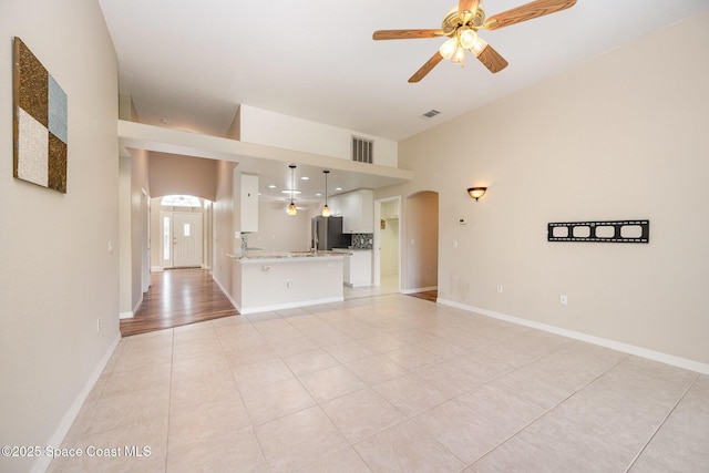 unfurnished living room featuring a ceiling fan, arched walkways, and baseboards