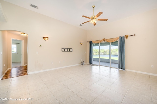 unfurnished room featuring arched walkways, light tile patterned floors, visible vents, a ceiling fan, and baseboards