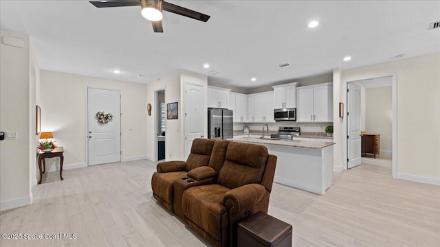 kitchen featuring white cabinets, an island with sink, appliances with stainless steel finishes, light stone counters, and light wood-type flooring