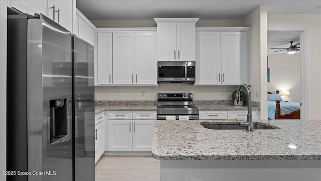 kitchen featuring appliances with stainless steel finishes, light wood-style floors, white cabinets, a sink, and light stone countertops