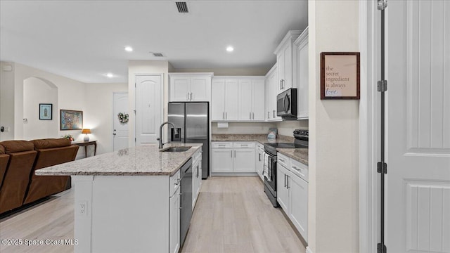 kitchen featuring light stone counters, white cabinetry, open floor plan, appliances with stainless steel finishes, and an island with sink