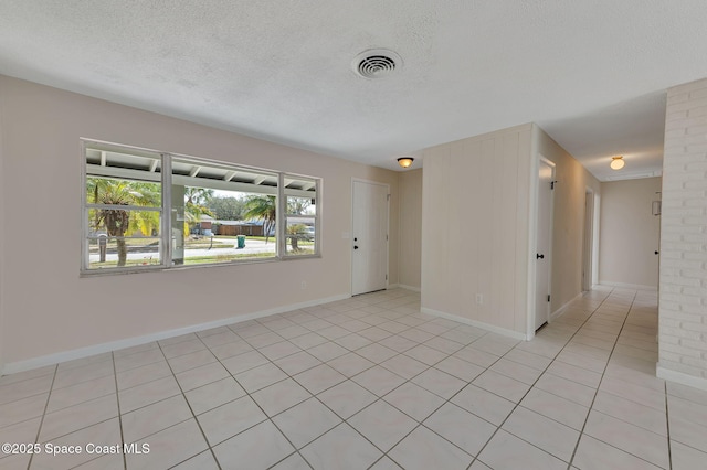 unfurnished room featuring a textured ceiling, light tile patterned floors, visible vents, and baseboards