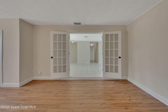 spare room with light wood finished floors, baseboards, visible vents, and french doors