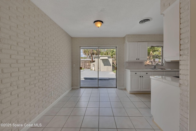 interior space with light tile patterned floors, light countertops, white cabinetry, a textured ceiling, and brick wall