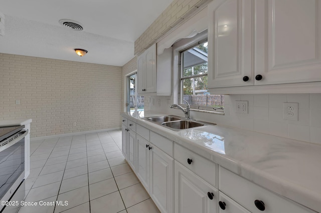 kitchen with stainless steel electric stove, light countertops, visible vents, a sink, and brick wall