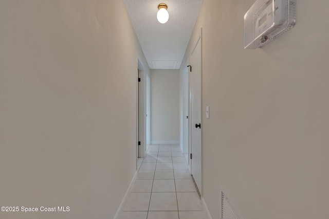 hall with a textured ceiling, light tile patterned floors, visible vents, and baseboards