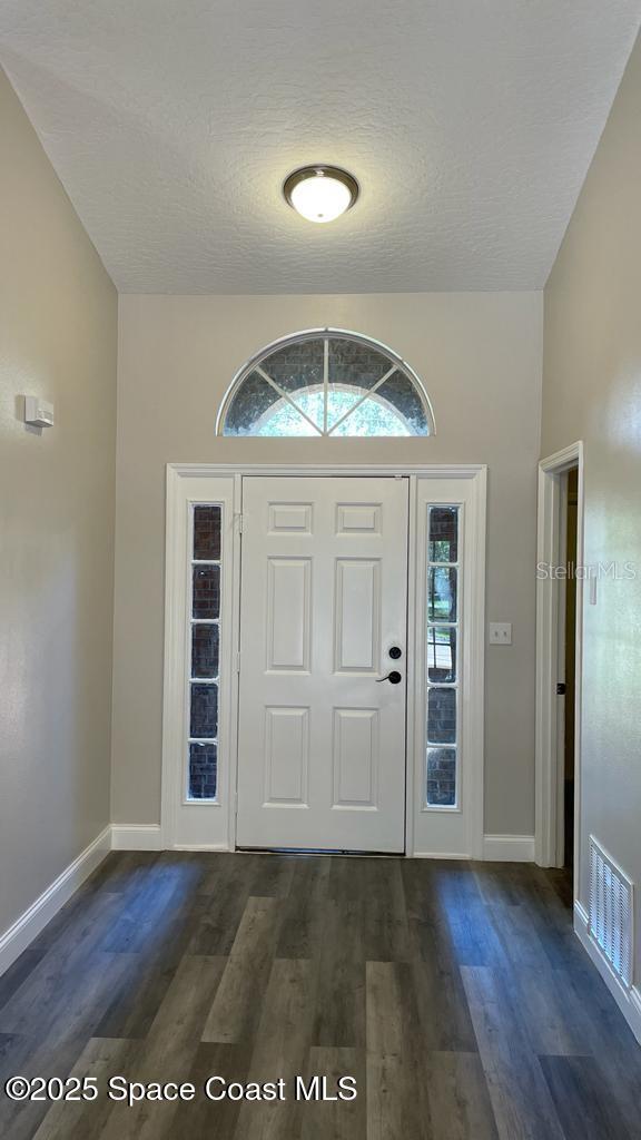 foyer featuring a textured ceiling, dark wood-style flooring, visible vents, and baseboards