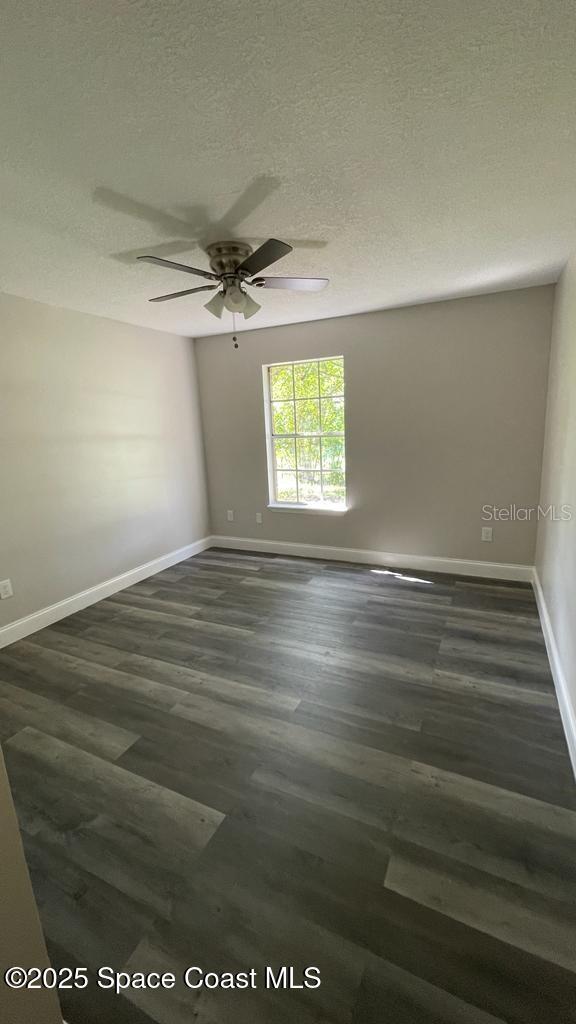 unfurnished room featuring a textured ceiling, ceiling fan, dark wood-type flooring, and baseboards