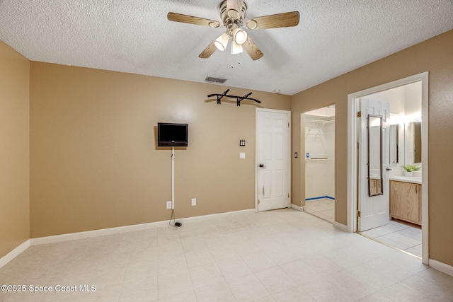 empty room featuring a ceiling fan, visible vents, a textured ceiling, and baseboards