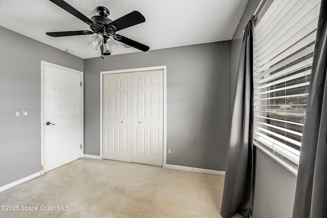 unfurnished bedroom featuring a closet, light colored carpet, a ceiling fan, a textured ceiling, and baseboards