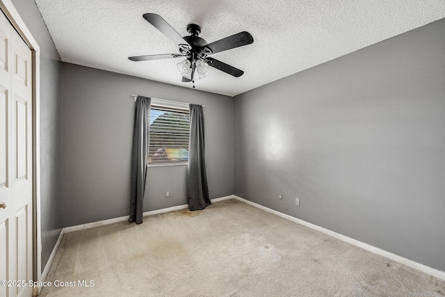 spare room with ceiling fan, baseboards, a textured ceiling, and light colored carpet