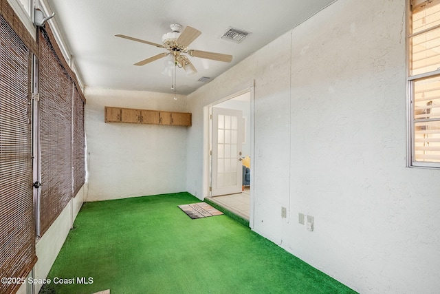 interior space featuring dark colored carpet, visible vents, a textured wall, and ceiling fan