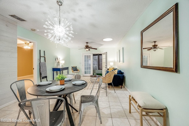 dining area with light tile patterned floors, a textured ceiling, wooden walls, a ceiling fan, and visible vents