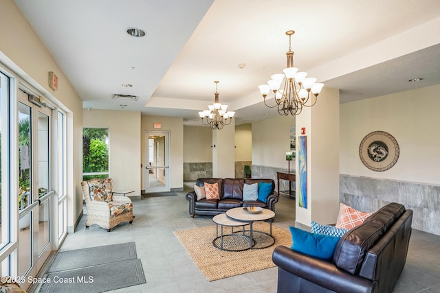 living area with visible vents, a raised ceiling, and a notable chandelier