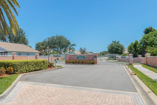 view of road featuring a gate, sidewalks, curbs, and a gated entry