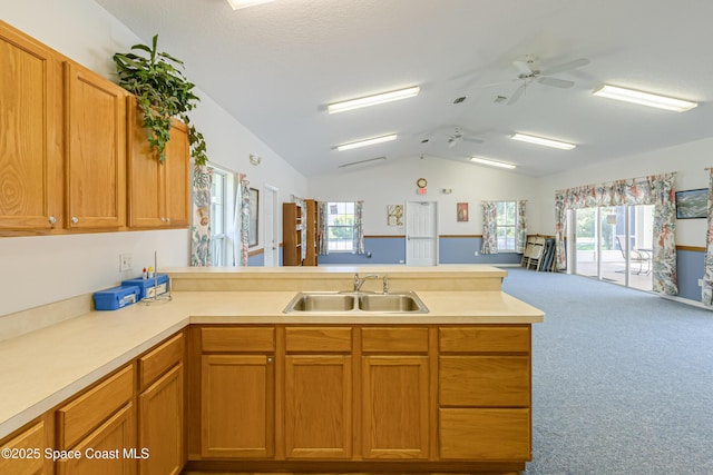 kitchen with a peninsula, a sink, open floor plan, vaulted ceiling, and light countertops