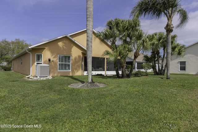 rear view of property featuring a lawn, central AC unit, and stucco siding