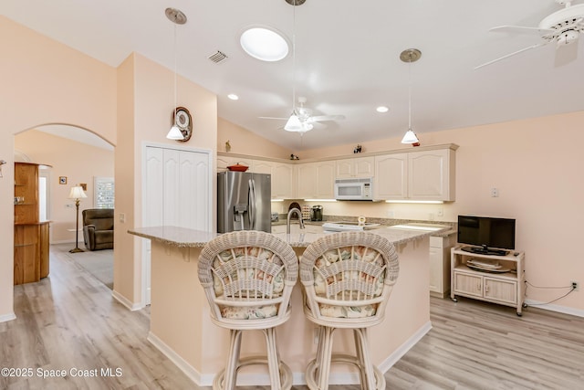 kitchen featuring arched walkways, white microwave, a ceiling fan, and stainless steel fridge with ice dispenser