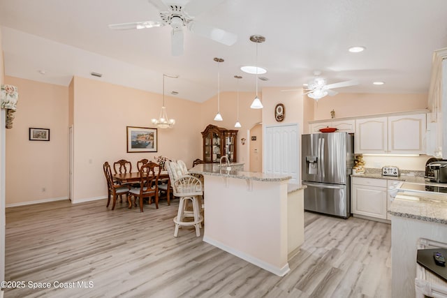 kitchen featuring stainless steel fridge, arched walkways, vaulted ceiling, light wood-style floors, and white cabinetry