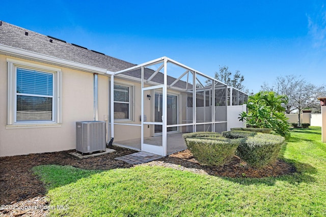 rear view of property with roof with shingles, stucco siding, central air condition unit, a lawn, and glass enclosure