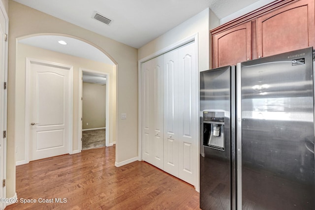 kitchen with stainless steel fridge, visible vents, arched walkways, baseboards, and light wood-type flooring