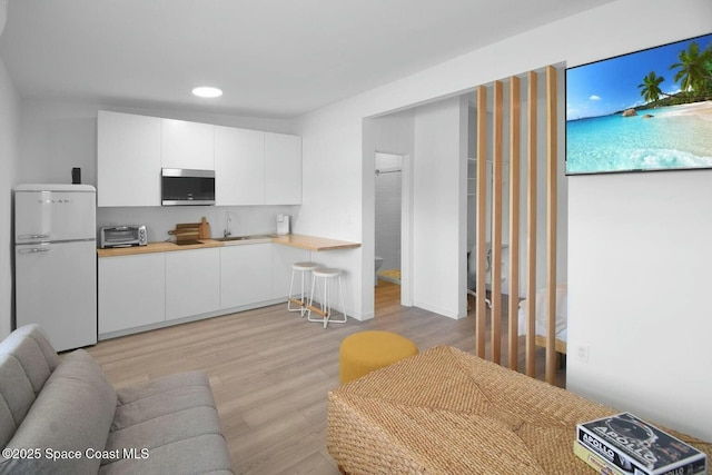 kitchen with a toaster, stainless steel microwave, light wood-style floors, freestanding refrigerator, and white cabinetry