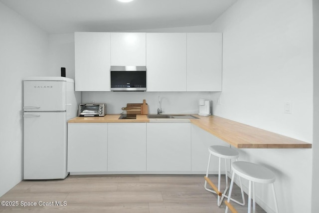 kitchen with butcher block counters, stainless steel microwave, freestanding refrigerator, white cabinetry, and a sink